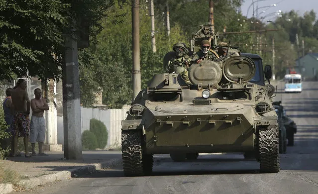 Pro-Russian rebels ride on an APC in the town of Krasnodon, eastern Ukraine, Sunday, August 17, 2014. A column of several dozen heavy vehicles, including tanks and at least one rocket launcher, rolled through rebel-held territory on Sunday. (Photo by Sergei Grits/AP Photo)