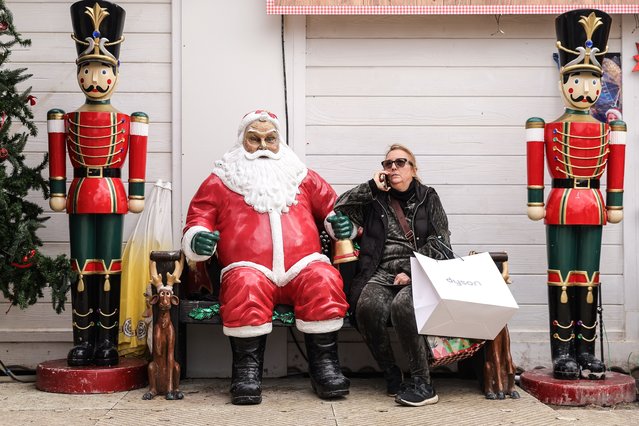 A woman rests with her shopping bags near a Santa Claus statue at the Christmas market in the Tuileries Garden in Paris, France, 23 December 2023. The market opened to the public on 18 November 2023 and runs through 07 January 2024. (Photo by Teresa Suarez/EPA)
