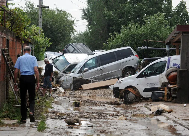 People walk through a street where cars have piled due to overnight flooding, after storms in the village of Stajkovci, just east of Skopje, Macedonia, Sunday, August 7, 2016. The Macedonian capital of Skopje has been hit Saturday night by torrential rain and floods that left at least 17 people dead, six missing and sent 60 others to the hospital. (Photo by Dragan Perkovski/AP Photo)