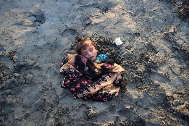 A girl sleeps while seen covered with sand in a beach by her parents with the believe that exposure during a solar eclipse will heal her illness, in Karachi on October 25, 2022. (Photo by Asif Hassan/AFP Photo)