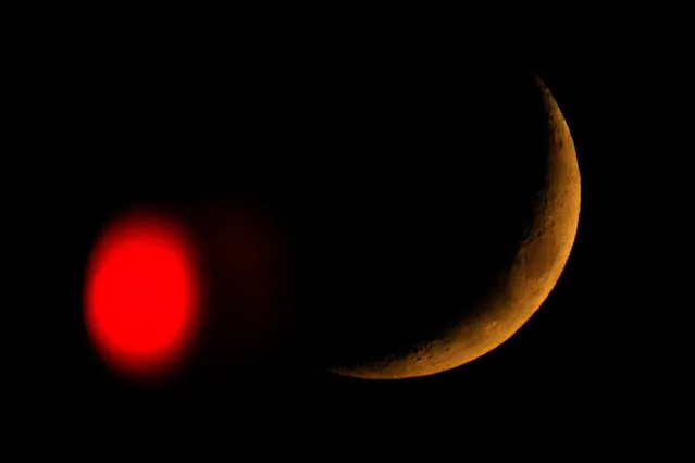 The crescent moon sets beyond a stop light in Overland Park, Kan., Friday, October 28, 2022. (Photo by Charlie Riedel/AP Photo)