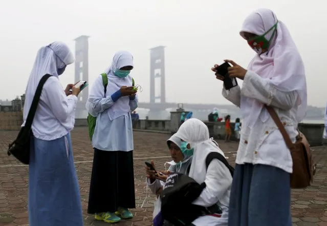 A group of Muslim students gather together as they use their smartphones in front of the haze shrouded Ampera Bridge in Palembang, on the Indonesian island of Sumatra, September 20, 2015. (Photo by Reuters/Beawiharta)