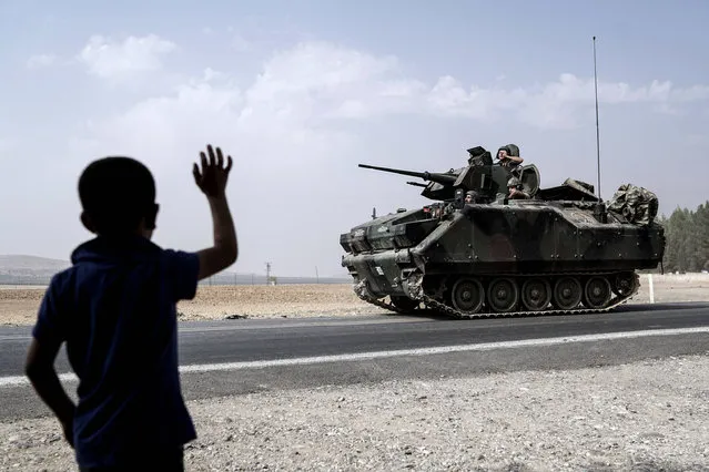 A child waves toward Turkish troops heading to the Syrian border, in Karkamis, Turkey, Friday, August 26, 2016. Turkey's state-run Anadolu news agency said late Thursday Turkish artillery have shelled a group of Syrian Kurdish militia fighters in the north of the town of Mambij after they allegedly ignored warnings to retreat. (Photo by Halit Onur Sandal/AP Photo)