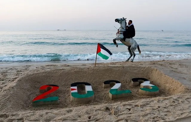 A Palestinian man rides his horse next to the 2023 drawing on the sand at the beach during the last sunset of 2022, in Gaza City on December 31, 2022. (Photo by Ibraheem Abu Mustafa/Reuters)