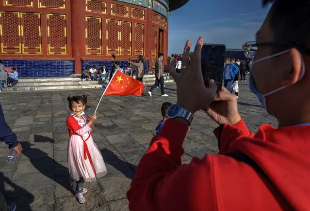 A Chinese girl holds a national flag as she has her photo taken by a relative as they visit the Temple of Heaven on October 2, 2020 during the national holiday in Beijing, China. China is celebrating its national day marking the 71st anniversary of the People's Republic of China and the Mid-autumn Festival for a week beginning on October 1st. (Photo by Kevin Frayer/Getty Images)