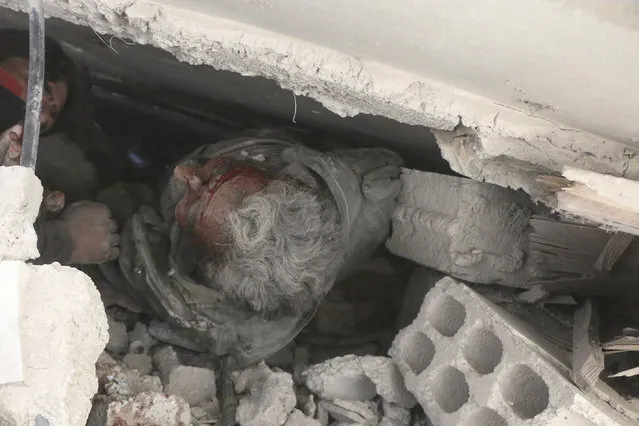 This photo released on Tuesday February 20, 2018 provided by the Syrian Civil Defense group known as the White Helmets, shows an injured man stuck under the rubble of a damaged building that attacked by Syrian government airstrike, in Ghouta, suburb of Damascus, Syria. A Syrian monitoring group and paramedics say government shelling and airstrikes on rebel-held suburbs of the capital, Damascus, killed at least 98 people on Monday. (Photo by Syrian Civil Defense White Helmets via AP Photo)