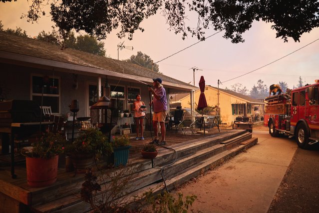 A home owner sprays down his house as firefighters battle the Canyon Fire in Castaic, California, 07 August 2025. (Photo by Allison Dinner/EPA)