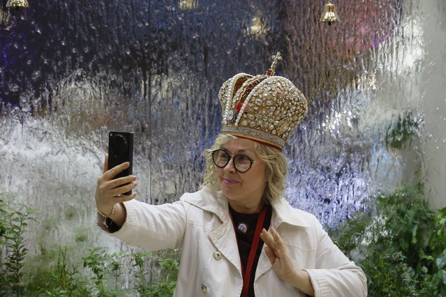 A participant poses with the Russian Imperial crown near an installation at the exhibition of the 28th St. Petersburg International Economic Forum (SPIEF) in St. Petersburg, Russia, 20 June 2025. The forum runs from 18 to 21 June 2025. (Photo by Anatoly Maltsev/EPA/EFE)