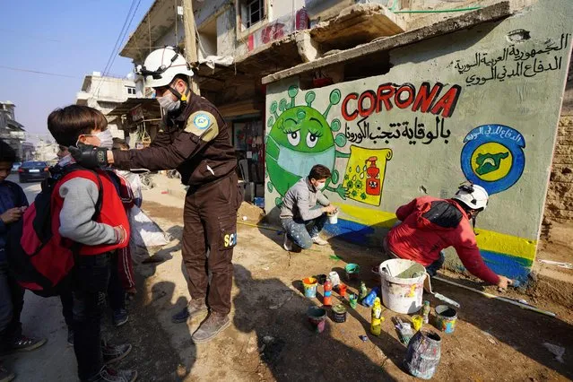 A member of the Syrian Civil Defence group known as the White Helmets instructs school children about the coronavirus during an awareness campaign organised on December 6, 2020 in the town of Binnish in Syria's northwestern Idlib province to inform children about the COVID-19 pandemic and protection methods against the contageous virus. (Photo by Muhammad Haj Kadour/AFP Photo)