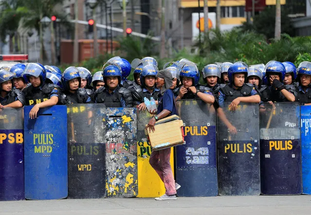 A vendor selling bottled water walks in front of riot police waiting for protesters outside the U.S. embassy in metro Manila, Philippines, October 27, 2016. (Photo by Romeo Ranoco/Reuters)