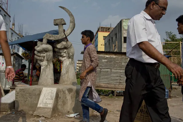 In this April 18, 2018 photo, Bangladeshi men walk past a monument erected in memory of victims of the Rana Plaza garment factory building collapse in Savar, Bangladesh. (Photo by A.M. Ahad/AP Photo)