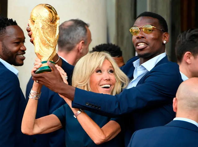 French President Emmanuel Macron' s wife Brigitte Macron (C) holds the trophy next to France' s midfielder Paul Pogba (R) during a reception at the Elysee Presidential Palace on July 16, 2018 in Paris, after French players won the Russia 2018 World Cup final football match. France celebrated their second World Cup win 20 years after their maiden triumph on July 15, 2018, overcoming a passionate Croatia side 4-2 in one of the most gripping finals in recent history. (Photo by Lionel Bonaventure/AFP Photo)