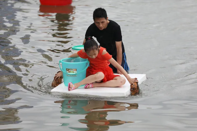 A girl, floating on a foam board, paddles with slippers as a man pushes the board through a flooded street, following heavy rainfall at a town in Shantou, Guangdong province, China on September 2, 2018. (Photo by Reuters/China Stringer Network)