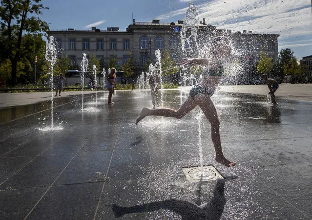 A girl cools off in a public fountain in Vilnius, Lithuania, Wednesday, August 16, 2023. The heat wave continues in Lithuania as temperatures rise to as high as 32 degrees Celsius (89.6 degrees Fahrenheit). (Photo by Mindaugas Kulbis/AP Photo)
