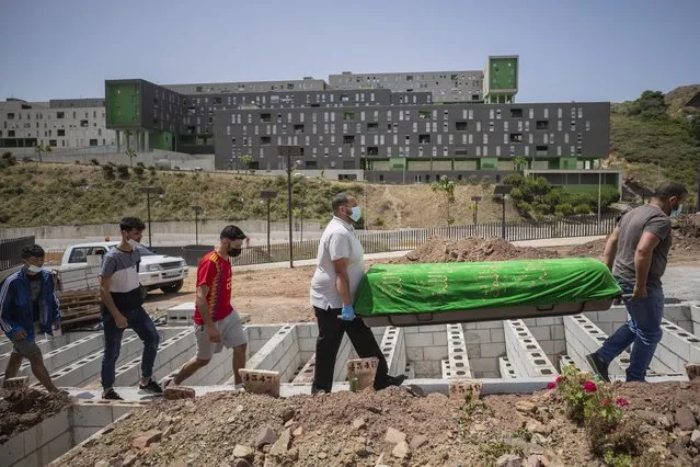 Funeral workers carry the body of a Moroccan teenager in the muslim cemetery of Ceuta, Saturday, May 22, 2021. The young man died on Monday 17 trying to swim across the border from Morocco to Spain's North Africa enclave together with thousands of other migrants. (Photo by Bernat Armangue/AP Photo)
