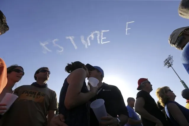 In this May 1, 2015  photo, Kevin Mueller, of Austin, Texas, kisses his wife Erin Mueller, as skywriter Nathan Hammond writes messages of hope and love over New Orleans, during the New Orleans Jazz & Heritage Festival. (Photo by Gerald Herbert/AP Photo)