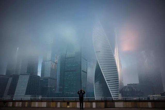 A pedestrian takes a picture of fog covered skyscrapers of Moscow's International Business Centre on November 2, 2021. (Photo by Dimitar Dilkoff/AFP Photo)
