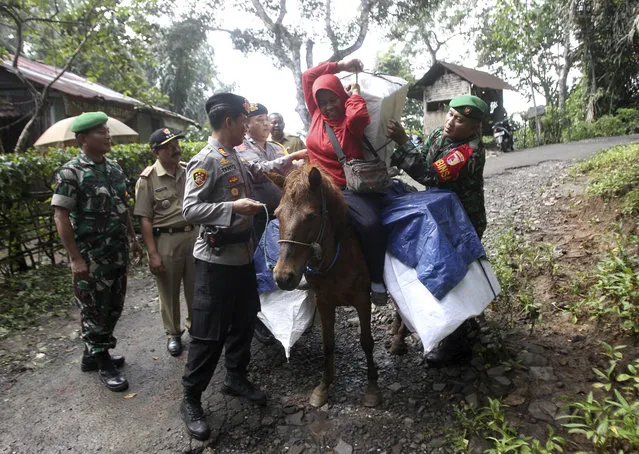 Police officers and soldiers assist a worker to carry ballot boxes and other election paraphernalia as they use horses to distribute them to polling stations in remote villages in Tempurejo, East Java, Indonesia, Monday, April 15, 2019. The world's third largest democracy is gearing up to hold its legislative and presidential elections that will pit the incumbent Joko Widodo against his contender former special forces general Prabowo Subianto. (Photo by AP Photo/Trisnadi)