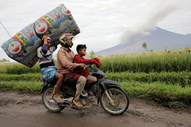 Locals transport a mattress on a motorcycle as Mount Semeru volcano continues to spew ash and smoke in the background following an eruption, in Gunung Sawur, Candipuro, Indonesia on December 7, 2021. (Photo by Willy Kurniawan/Reuters)