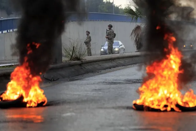Lebanese army soldiers stand in front of burning tires blocking a main highway that leads to Beirut's international airport during a protest against the increasing prices of consumer goods and the crash of the local currency in Beirut, Lebanon, Monday, November 29, 2021. (Photo by Hussein Malla/AP Photo)