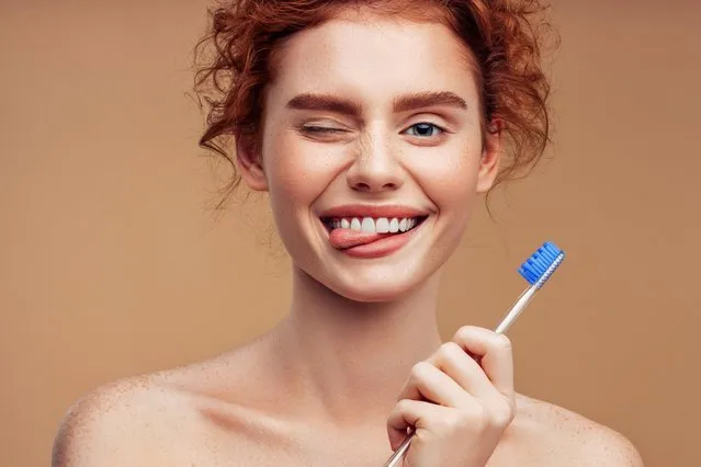 A close up of a person holding a toothbrush, beautiful redhead woman, tan complexion, happy girl. (Photo by Matija Jama/Rex Features/Shutterstock)