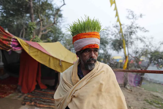 A Hindu devotee with wheat growing on his headgear stands at the Sangam, the confluence of three rivers – the Ganges, the Yamuna and the mythical Saraswati, to take a ritualistic bath during Makar Sankranti festival that falls during the annual traditional fair of Magh Mela festival, one of the most sacred pilgrimages in Hinduism, in Prayagraj, India. Friday, January 14, 2022. (Photo by Rajesh Kumar Singh/AP Photo)