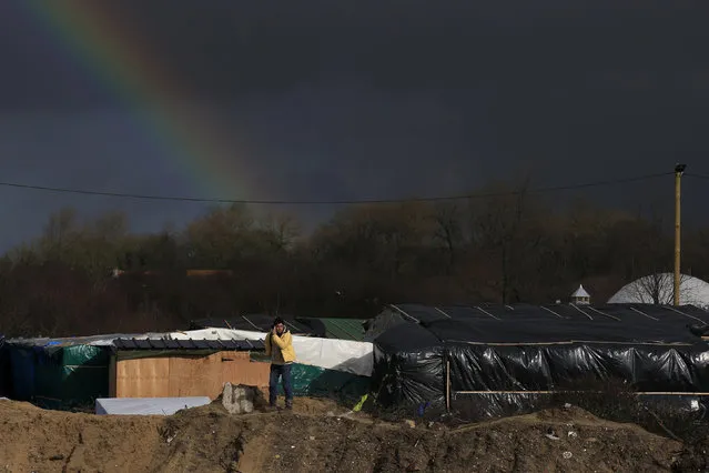 A rainbow is seen over the “Jungle” as a migrant stands on top of a pile of sand which separates the road that leads to the ferry terminal and a squalid sprawling camp in Calais, northern France, February 15, 2016. (Photo by Pascal Rossignol/Reuters)