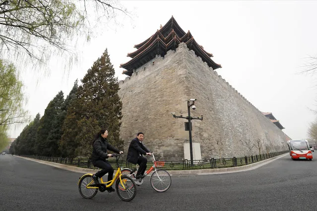 In this Wednesday, March 22, 2017 photo, people ride bicycles of bike-sharing companies Ofo, left,  and Mobike, right,  past a corner tower of the Forbidden City in Beijing, China. As many as 2.2 million of these two-wheelers have been deployed, which are available for rent for as little as U.S. 7 cents for half an hour, in the latest symbol of heavy spending in China's internet sector where startups are in a race to attract more users to their services. (Photo by Andy Wong/AP Photo)