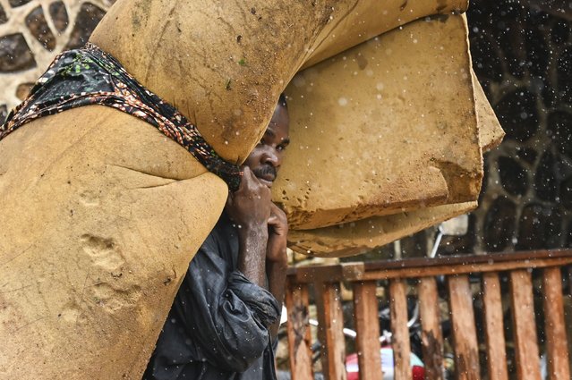 A man carries his belongings at a displacement center in Blantyre, Malawi Tuesday March 14, 2023. The unrelenting Cyclone Freddy that is currently battering southern Africa has killed more than 50 people in Malawi and Mozambique since it struck the continent for a second time on Saturday night. (Photo by Thoko Chikondi/AP Photo)