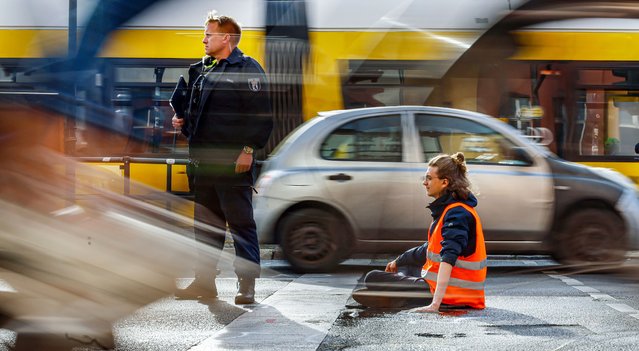 A police officer stands guard as vehicles drive past a Letzte Generation (Last Generation) climate activist who glued his hand to the asphalt during a climate protest in Berlin, Germany, 22 May 2023. The activists gathered to demand climate councils, the enforcement of speed limits on all German highways and affordable public transport. (Photo by Hannibal Hanschk/EPA/EFE/Rex Features/Shutterstock)