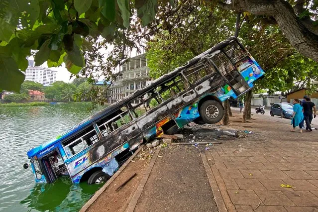 People walk past a burnt bus near Sri Lanka's former prime minister Mahinda Rajapaksa's official residence, a day after it was torched by protesters in Colombo on May 10, 2022. Five people were killed and more than 225 wounded in a wave of violence in Sri Lanka where the prime minister resigned after weeks of protests over the worsening economic crisis. (Photo by Ishara S. Kodikara/AFP Photo)