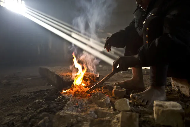 In this Monday, January 30, 2017 photo, unaccompanied minor Obaidullah, 14, a migrant from Wardak, Afghanistan, warms his legs and hands around a fire in an abandoned warehouse where he and other migrants took refuge in Belgrade, Serbia. (Photo by Muhammed Muheisen/AP Photo)