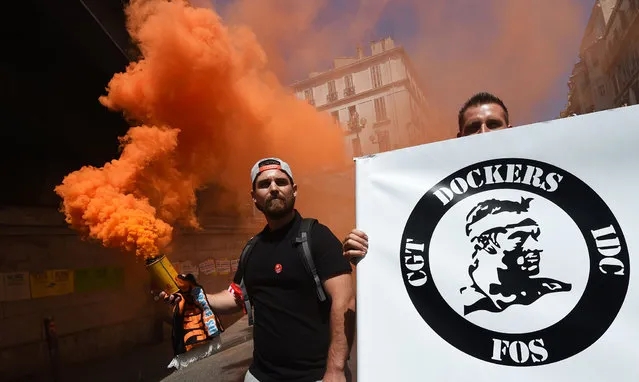 Protestors hold a smoke bomb and a placard of the French General Confederation of Labour (CGT) worker's union of the dockers branch during a demonstration against the French government's planned labour law reforms on June 23, 2016 in Marseille, southern France. Unions are protesting a series of labour market reforms that Valls had to force through parliament in May to avoid a vote, even after the bill was significantly watered down. However after more than three months of protests and strikes over the legislation, neither side is willing to budge. (Photo by Anne-Christine Poujoulat/AFP Photo)