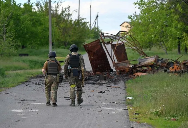 Ukrainian servicemen walk next to a destroyed military in the village of Rus'ka Lozova, north of Kharkiv, on May 28, 2022, amid Russian invasion of Ukraine. (Photo by Genya Savilov/AFP Photo)