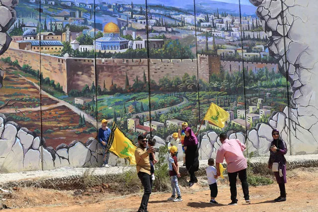 Hezbollah supporters wave Hezbollah flags in front of a poster shows the Dome of the Rock Mosque in the Al Aqsa Mosque painted on a wall that build by Israel, at the Lebanese-Israeli border, as they mark “Liberation Day” the twenty second anniversary of Israel's withdrawal from southern Lebanon in May 25, 2000, in Kfar Kila village, Southern Lebanon, Wednesday, May 25, 2022. (Photo by Mohammed Zaatari/AP Photo)