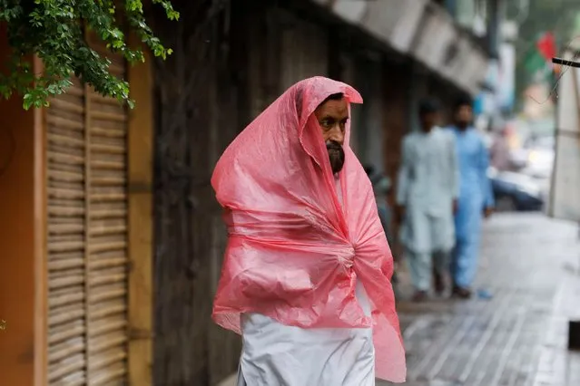 A man, covered with a plastic sheet to avoid rain, walks along a sidewalk during the monsoon season, in Karachi, Pakistan on July 24, 2022. (Photo by Akhtar Soomro/Reuters)