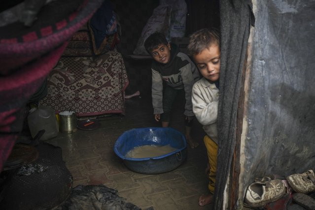 Brothers Belal, 5, and Mohammed Hamad, 7, collect water from their flooded family tent after overnight rainfall at the refugee tent camp for displaced Palestinians in Deir al-Balah, central Gaza Strip, Tuesday, December 31, 2024. (Photo by Abdel Kareem Hana/AP Photo)
