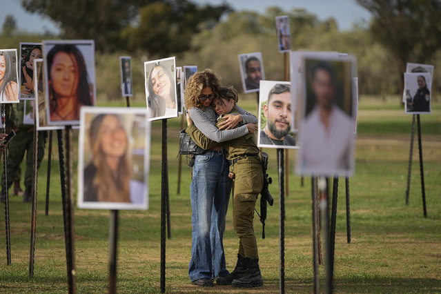 Israelis embrace next to photos of people killed and taken captive by Hamas militants during their violent rampage through the Nova music festival in southern Israel, which are displayed at the site of the event, as Israeli DJs spun music, to commemorate the October 7, massacre, near kibbutz Re'im, Tuesday, November 28, 2023. (Photo by Ohad Zwigenberg/AP Photo)