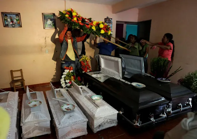 People carry a floral wreath next to coffins of relatives killed after a mudslide, in the aftermath of Tropical Storm Earl in the town of San Miguel Xaltepec, in Puebla state, Mexico, August 8, 2016. (Photo by Henry Romero/Reuters)