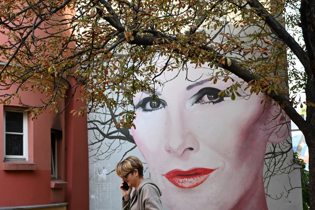 A woman speaks on her mobile phone as she walks past a mural by Polish artist Bruno Althamer, depicting late Polish rock singer Olga Sipowicz, also known as Kora, during a sunny autumn day in Warsaw on September 17, 2024. Kora died of cancer in 2018 having lost her hair, but this mural gives her an opportunity to change hairstyle every season, the artist explained his idea behind the work. (Photo by Sergei Gapon/AFP Photo)