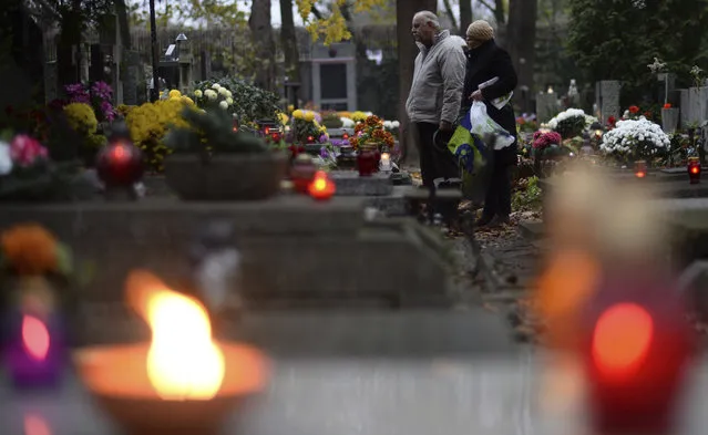 People stop in front of a grave at the Powazki cemetery in Warsaw, Poland, Wednesday, November 1, 2017. Candles and flowers cover tombstones in graveyards across Poland on All Saints' Day, as people honour the saints and their departed friends and family, in Christian tradition. (Photo by Alik Keplicz/AP Photo)