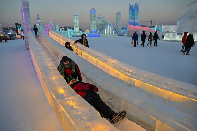 People slide down in an ice slide at the Harbin Ice and Snow World in Harbin, in China's northeastern Heilongjiang province, on January 5, 2023, during the opening ceremony of the 39th Harbin China International Ice and Snow Festival. (Photo by Hector Retamal/AFP Photo)