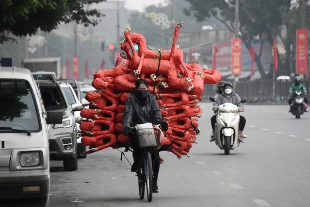 A woman carries horse figurines, to be used as offerings at religious ceremonies, on her bicycle as she transports them to shops for sale in Hanoi on January 11, 2023. (Photo by Nhac Nguyen/AFP Photo)