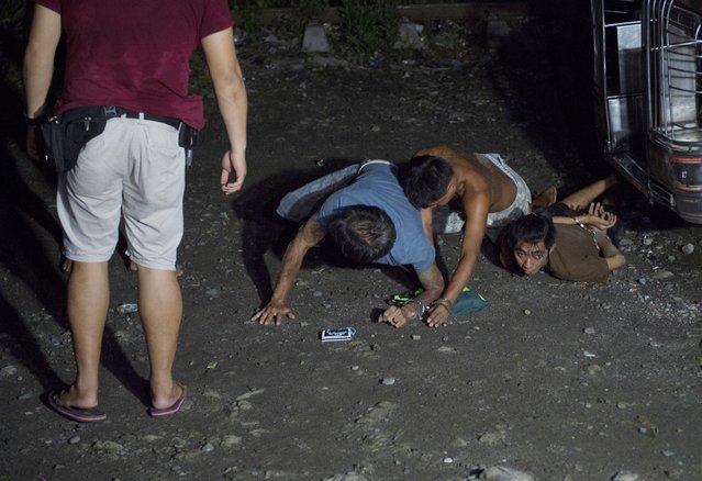 A police officer (L) wathces over suspected drug users arrested during a drug buy-bust operation by police along a rail line in Caloocan City suburban Manila on early September 30, 2016. (Photo by Ted Aljibe/AFP Photo)