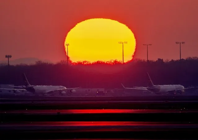 Parked aircrafts are seen at the airport in Frankfurt, Germany, as the sun rises on Tuesday, March 22, 2022. Security employees controlling passengers and luggage are on a one day lasting strike for higher wages. (Photo by Michael Probst/AP Photo)