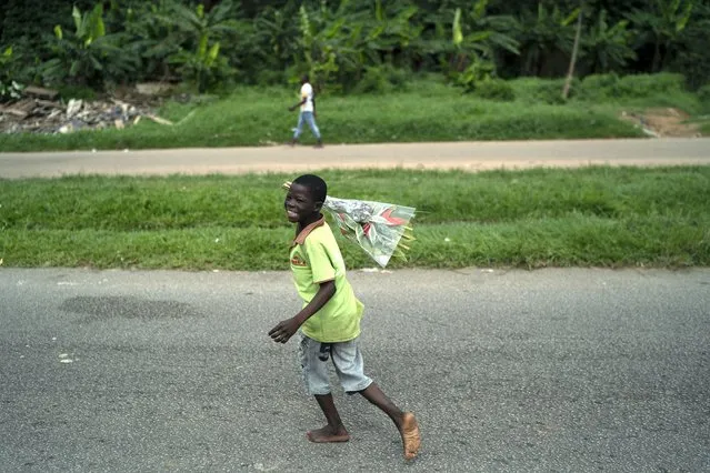 A child holds up a bouquet of flowers to sell as he waits for a customer, at the entrance of a cemetery during the Day of the Dead celebrations in Abidjan, Ivory Coast, Monday, November 2, 2020. (Photo by Leo Correa/AP Photo)