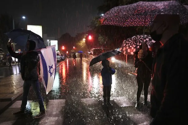Israelis stand with umbrellas under the rain during a protest against the government's plans to overhaul the country's legal system, in Tel Aviv, Israel, Saturday, January 14, 2023. Tens of thousands of Israelis have gathered in central Tel Aviv to protest plans by Prime Minister Benjamin Netanyahu's new government to overhaul the country's legal system and weaken the Supreme Court. (Photo by Oded Balilty/AP Photo)