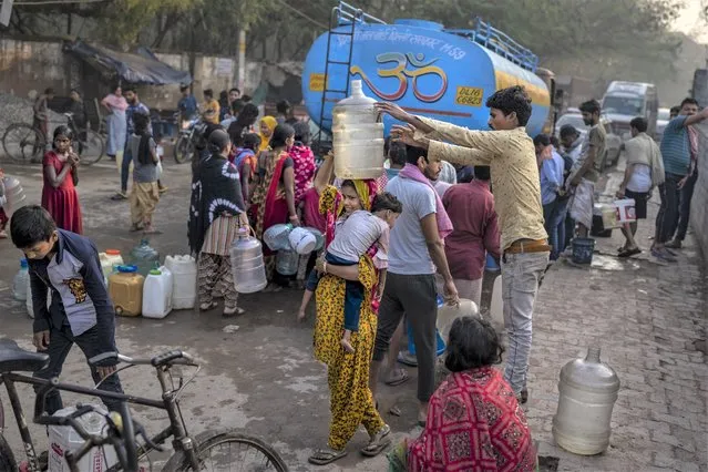 A woman balances a water can on her head while carrying a child as people collect water from a mobile water tanker on World Water Day in a residential area in New Delhi, India, March 22, 2023. (Photo by Altaf Qadri/AP Photo)