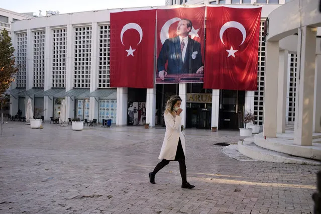 A woman wearing a mask to help protect against the spread of coronavirus, walks past a shopping center decorated with national flags and a poster of modern Turkey's founder, Mustafa Kemal Ataturk, as the nation remember the founding father on the 82nd anniversary of his death, in Ankara, Turkey, Wednesday, November 11, 2020. Turkey's government had urged the residents of big cities to limit their mobility and called on employers to offer workers flexible or staggered working hours and the possibility of working from homes. (Photo by Burhan Ozbilici/AP Photo)