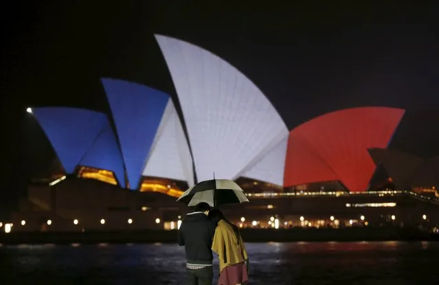 A couple stands in the rain as the blue, white and red colours of France's national flag are projected onto the sails of Sydney's Opera House in Australia November 14, 2015 following the attacks in Paris. (Photo by Jason Reed/Reuters)